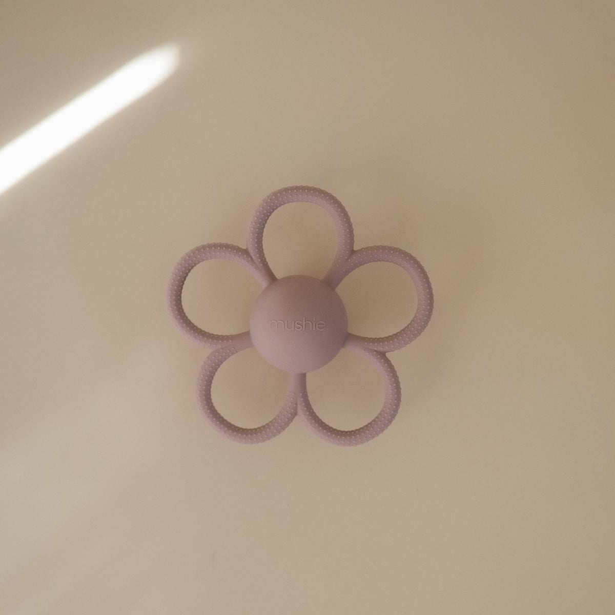 Mushie Daisy Rattle Teether, a soft silicone daisy-shaped baby toy.