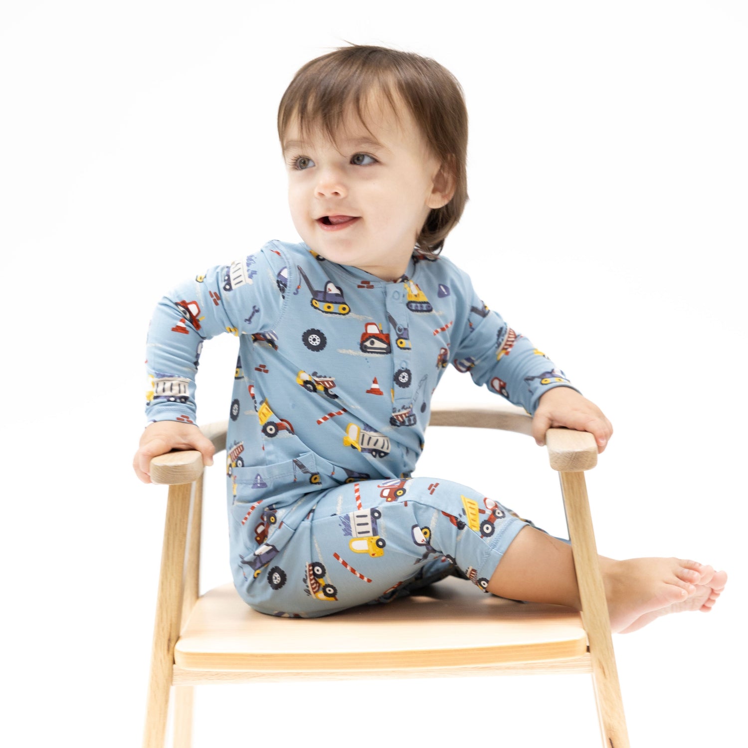 Baby romper in a crayon-style construction truck print with a Henley neckline and snap closures.
