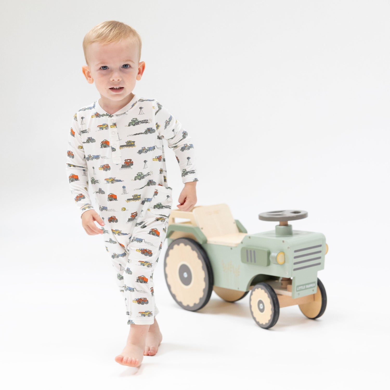 Baby romper in a farm machines print with tractors, a henley neckline, and snap closures