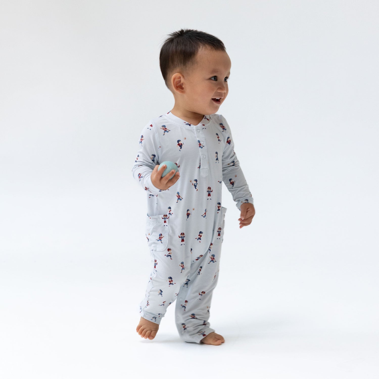 Baby romper with tiny footballs print, henley neckline, and snap closures along the legs.