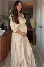 Cream floral maternity maxi dress with sweetheart neckline, empire waist, and flutter sleeves worn by a pregnant woman.
