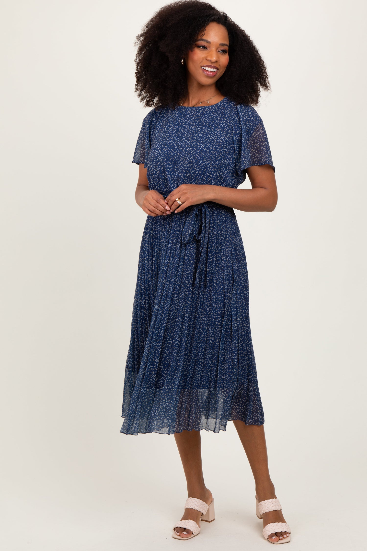 Navy leaf print pleated midi dress with short sleeves, crew neckline, and adjustable waist tie, styled with heels.