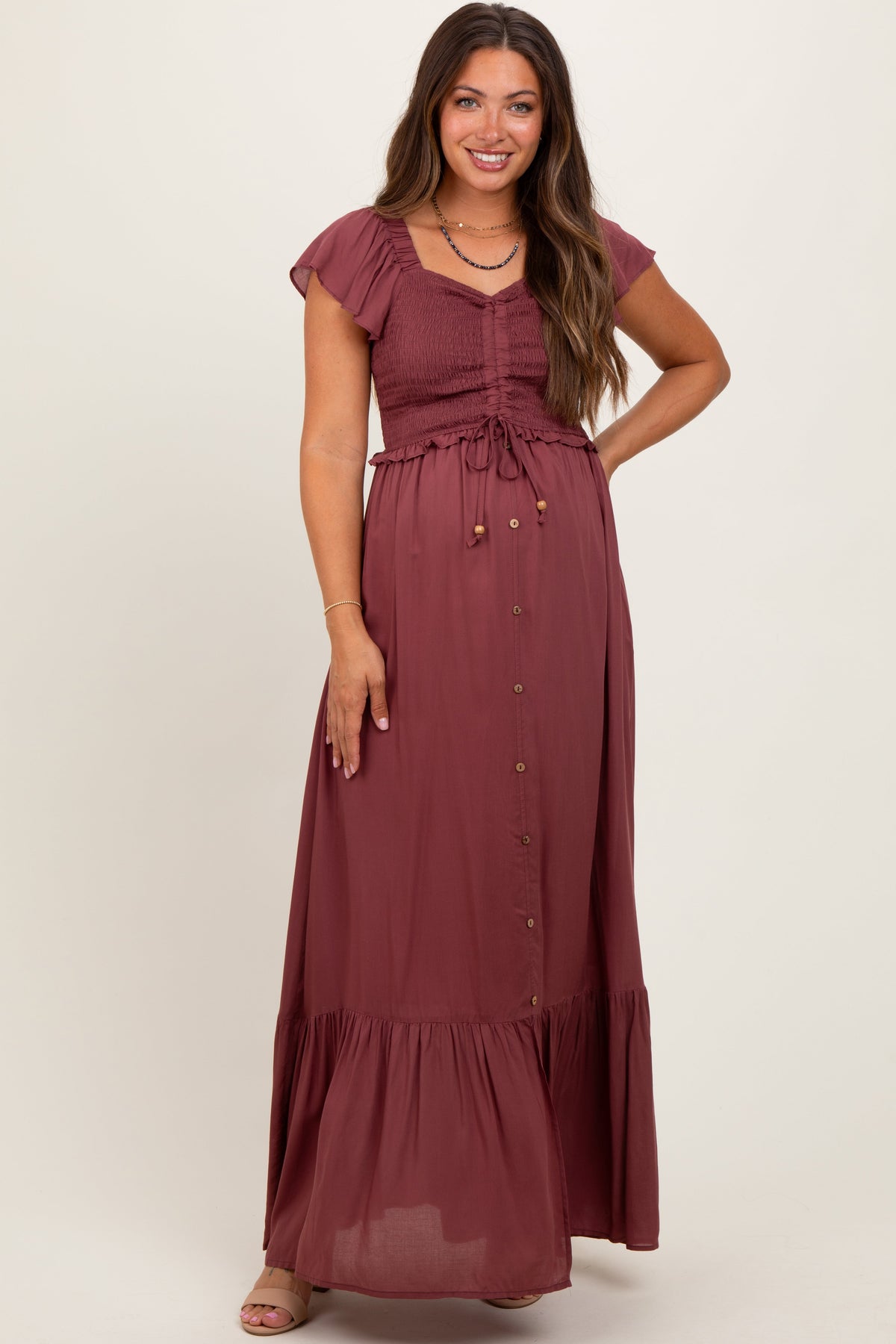 Burgundy maternity maxi dress with a smocked bodice and long flowing woven skirt worn by a pregnant woman.