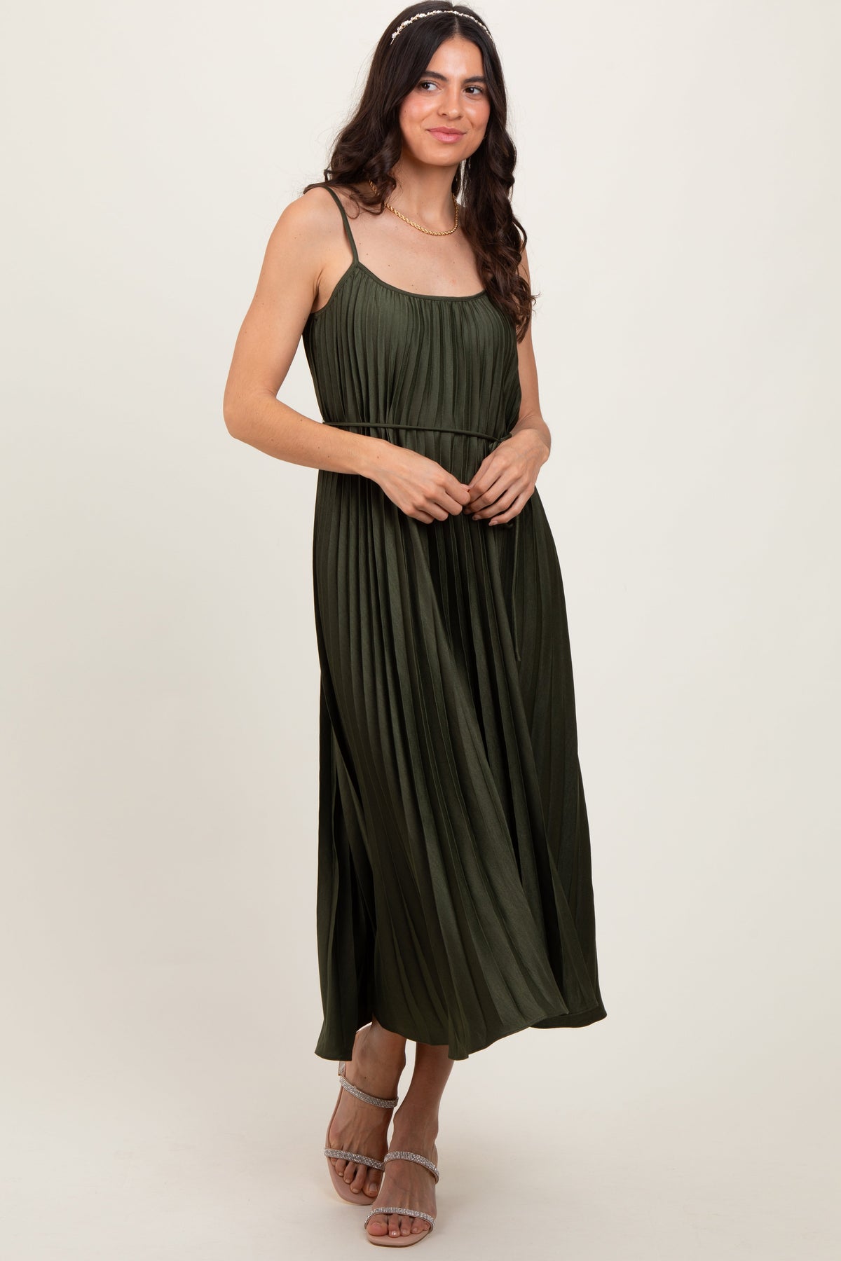 Olive pleated midi dress with spaghetti straps and a tie sash at the waist, styled with heels.