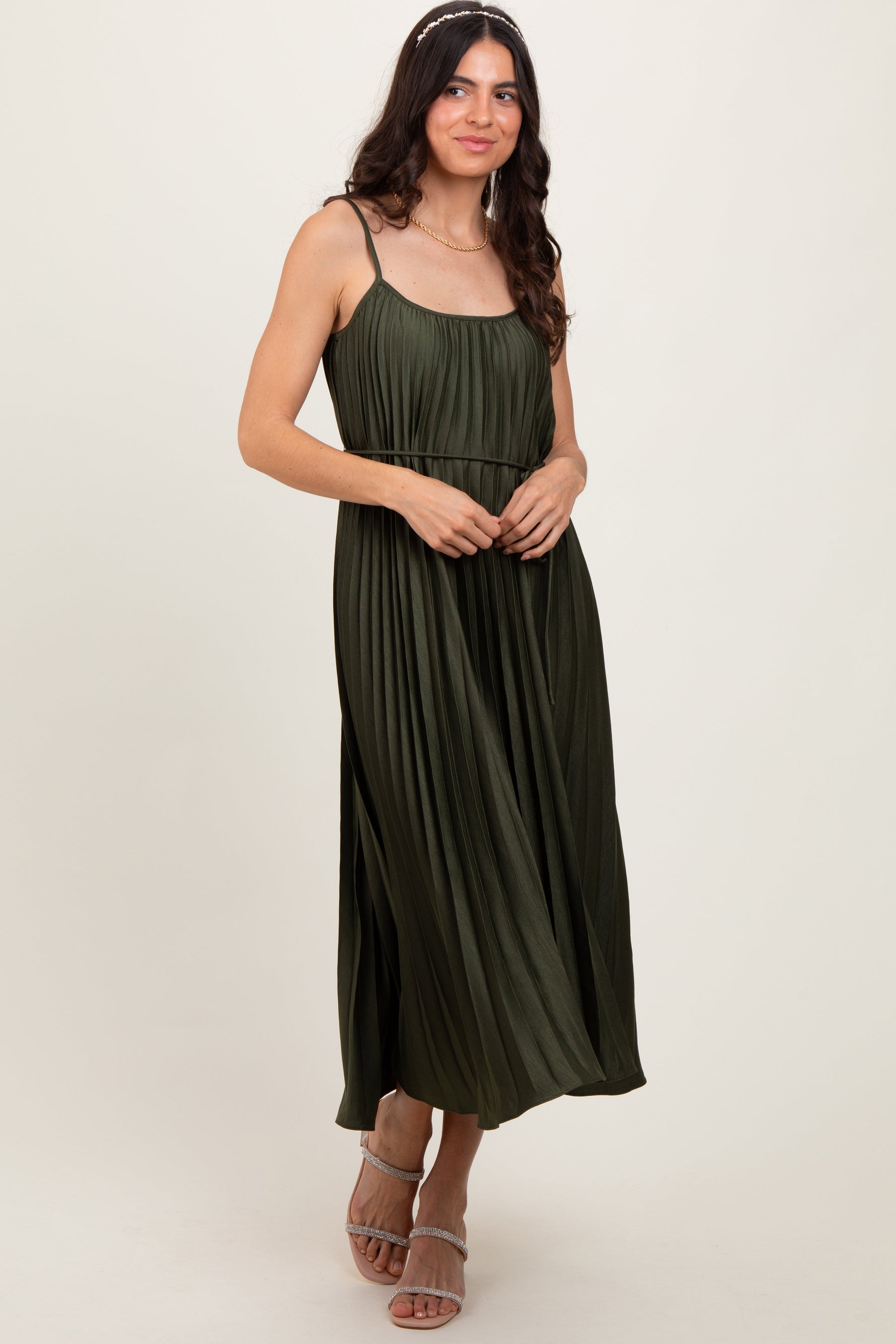 Olive pleated midi dress with spaghetti straps and a tie sash at the waist, styled with heels.
