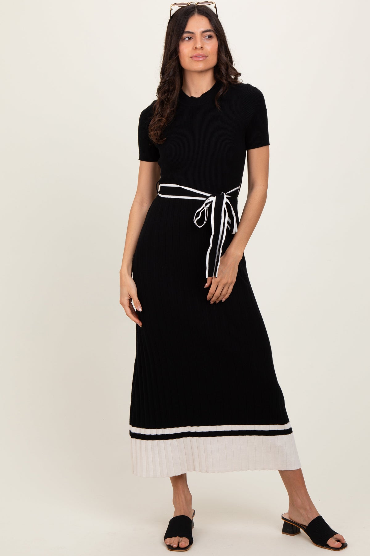 Black ribbed knit midi dress with mock neck, short sleeves, pleated skirt, and white stripe tie belt at the waist.