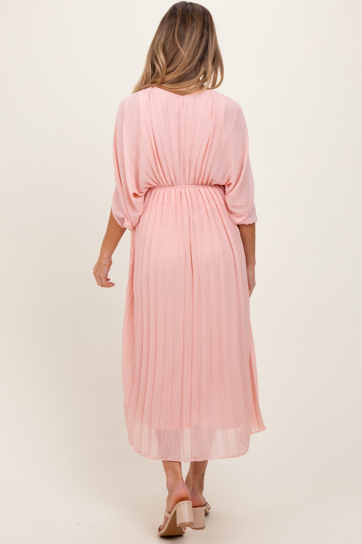 Light pink pleated V-neck maxi dress for maternity, worn by an expecting mother, standing gracefully.