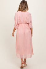 Light pink pleated V-neck maxi dress for maternity, worn by an expecting mother, standing gracefully.