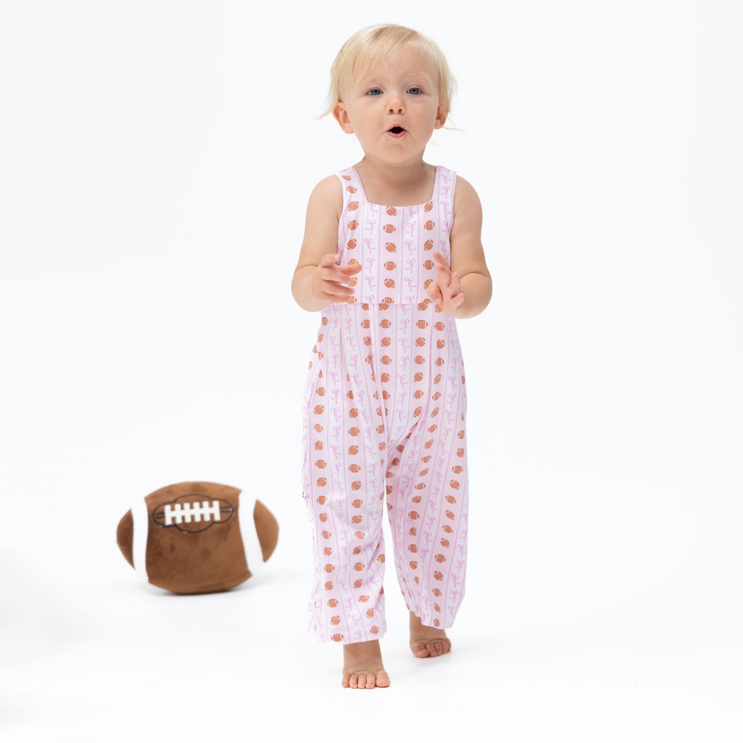 Wide leg baby jumpsuit in a football bow stripe pattern with snap closures at the legs.