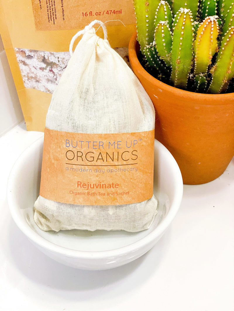 Organic rejuvenating bath tea sachet in a white bowl with a clay pot and cactus in the background.