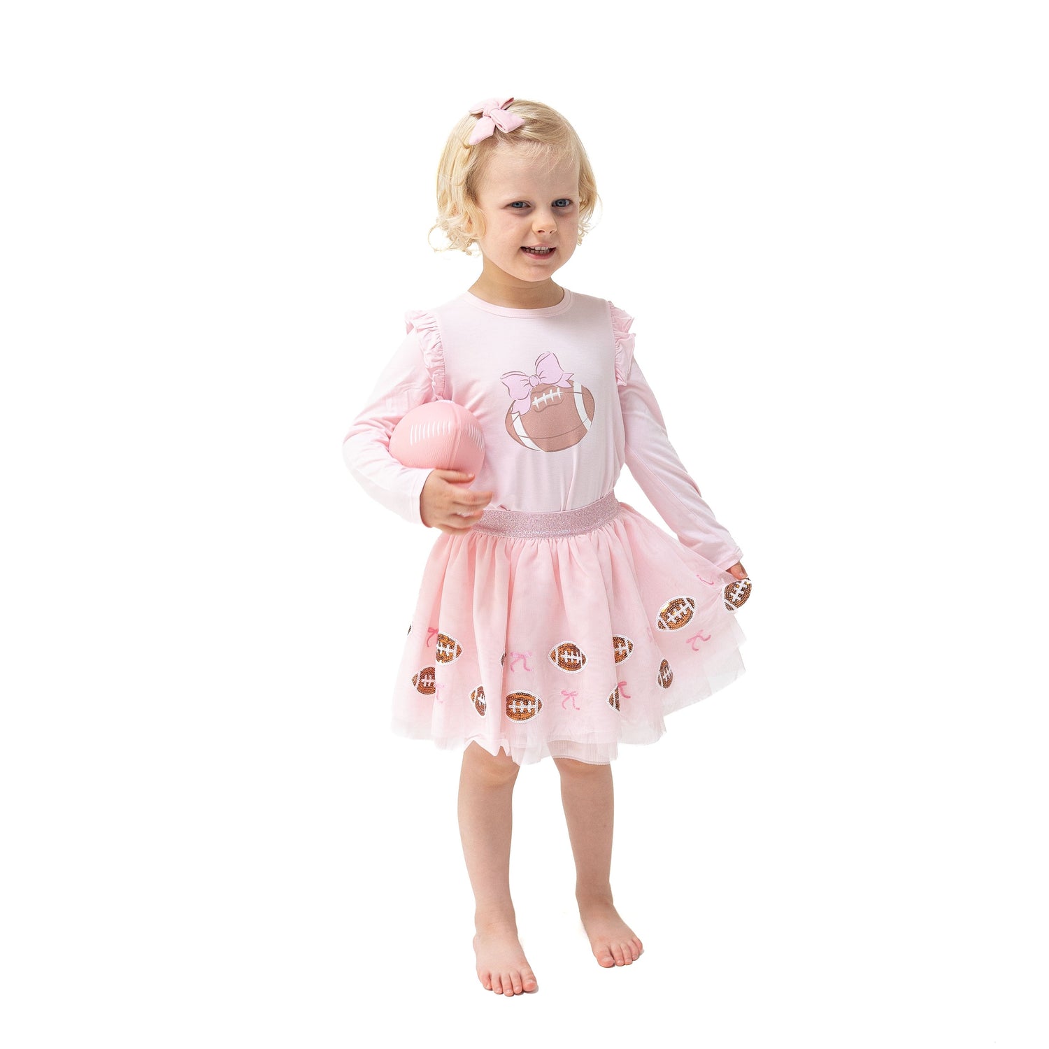 Pink long sleeve tee with ruffle shoulders and a glittery football with a bow screenprint