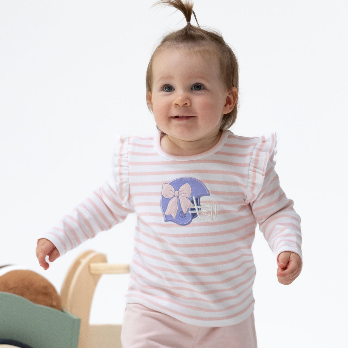 Pink long sleeve baby tee with purple football helmet applique and ruffle detail at the shoulders