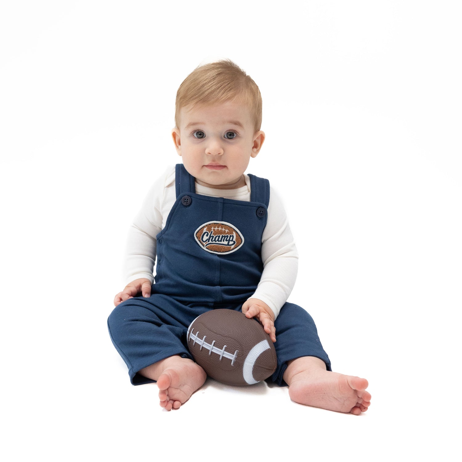 French terry baby overalls with a football and "Champ" appliqué, button straps, and snap-up legs.
