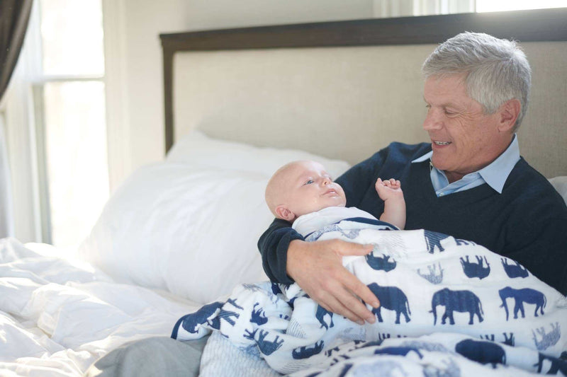 Newcastle Classics blue elephant and spotted wave muslin blanket on a bed with a baby and adult.