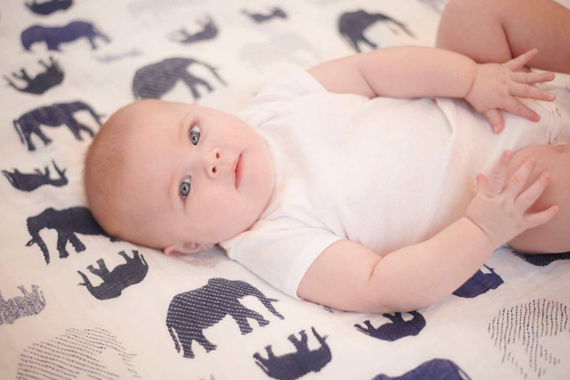 Blue elephant and spotted wave Newcastle Classics blanket with a baby lying on it, made of soft natural cotton muslin.