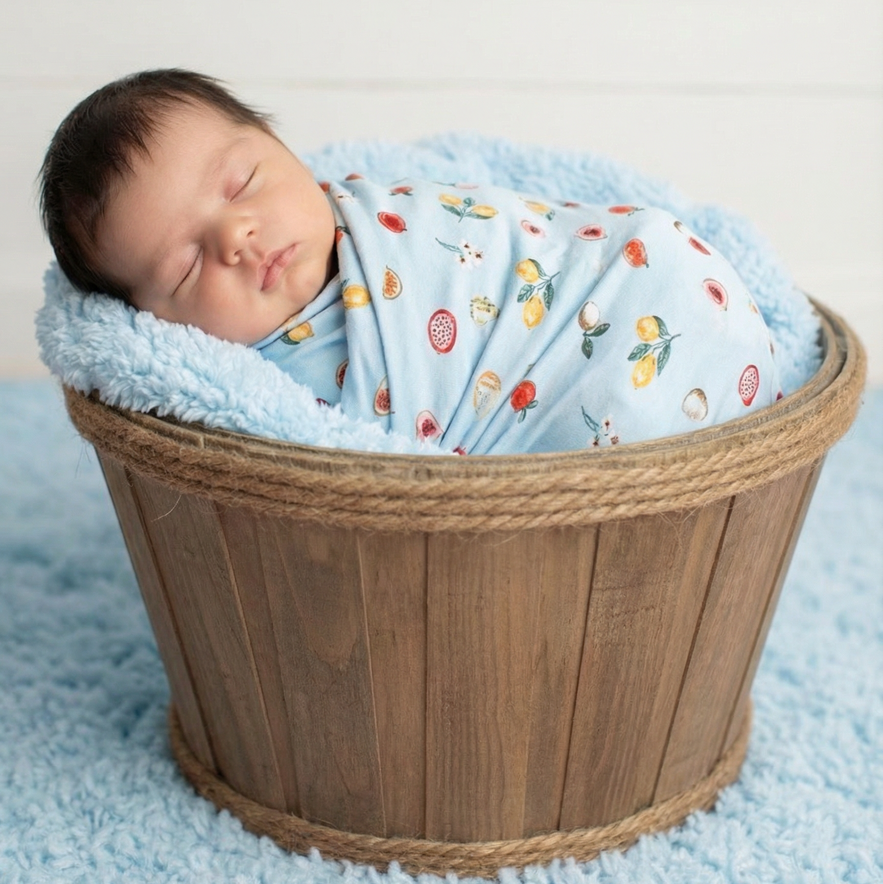 Baby swaddle blanket with colorful fruit print, shown folded in a wicker basket