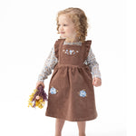 Corduroy pinafore dress with blue embroidered flowers layered over a long sleeve baby bodysuit