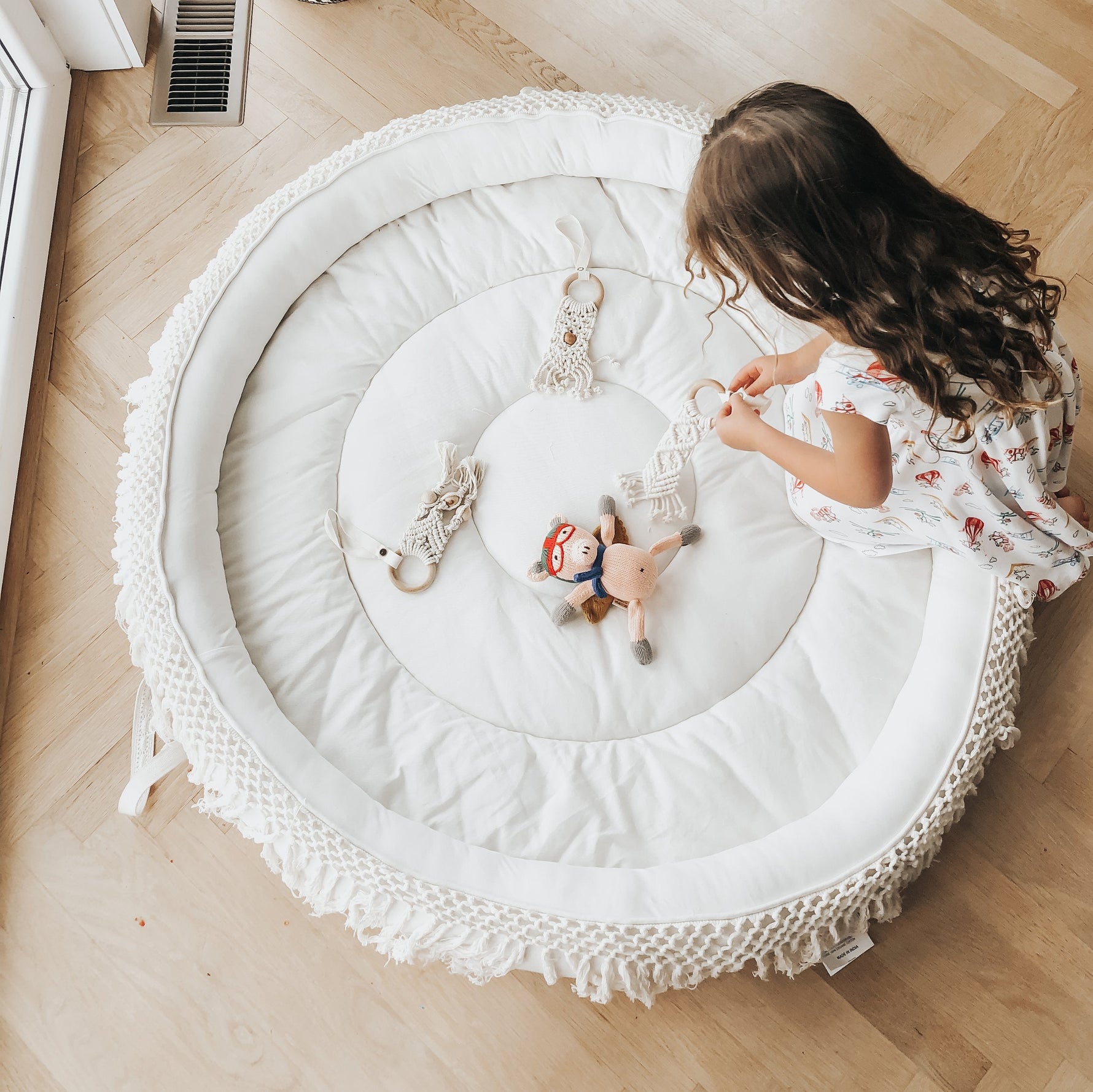 Finn + Emma organic macrame round play mat on a nursery floor, with a baby happily playing.