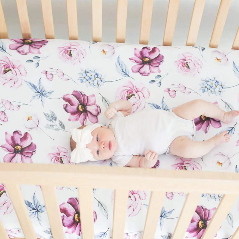 Vintage floral fitted crib sheet with baby lying in wooden crib.