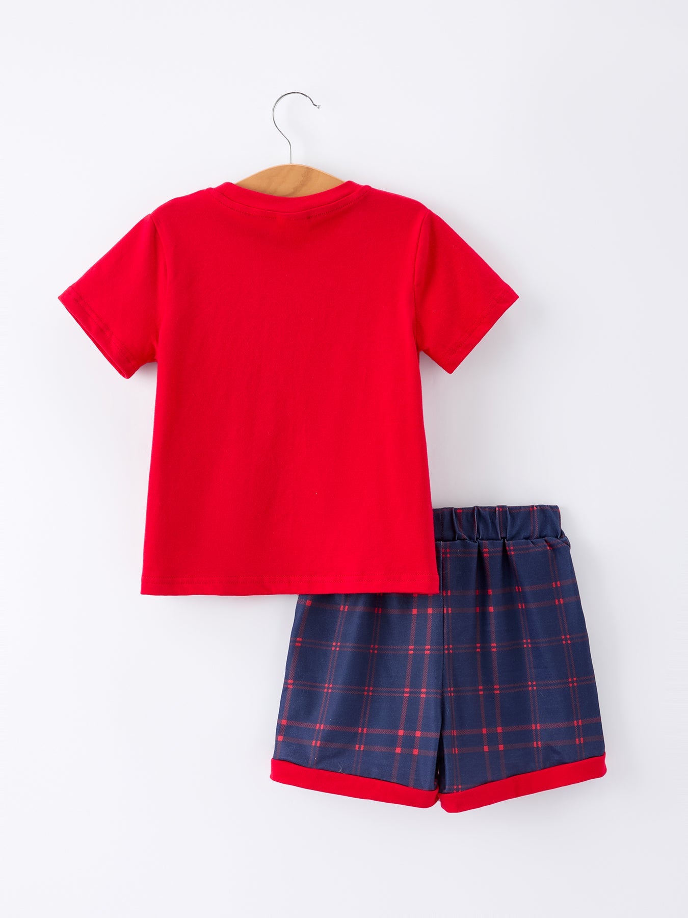 Young boy wearing a red apple graphic t-shirt and blue plaid shorts, smiling, ready for school.