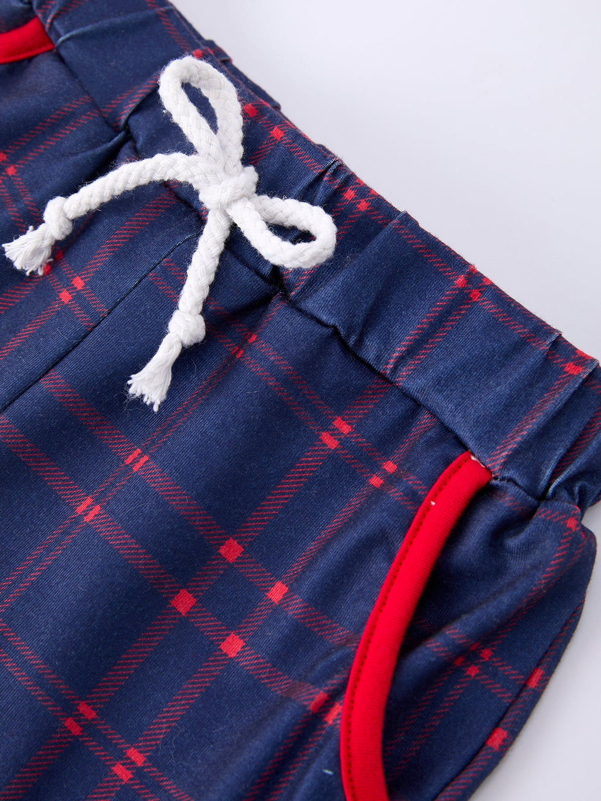 Young boy wearing a red apple graphic t-shirt and blue plaid shorts, smiling, ready for school.