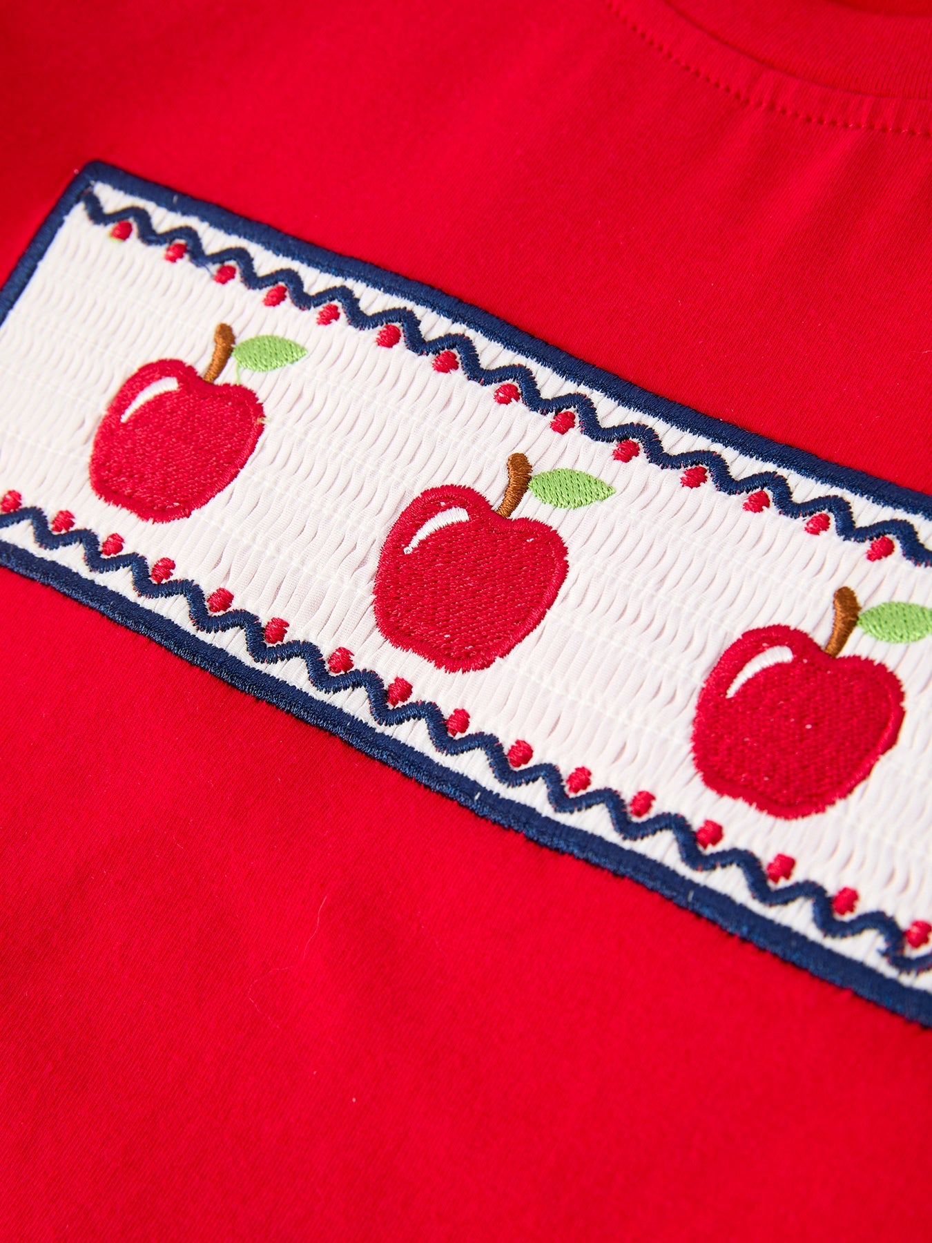 Young boy wearing a red apple graphic t-shirt and blue plaid shorts, smiling, ready for school.