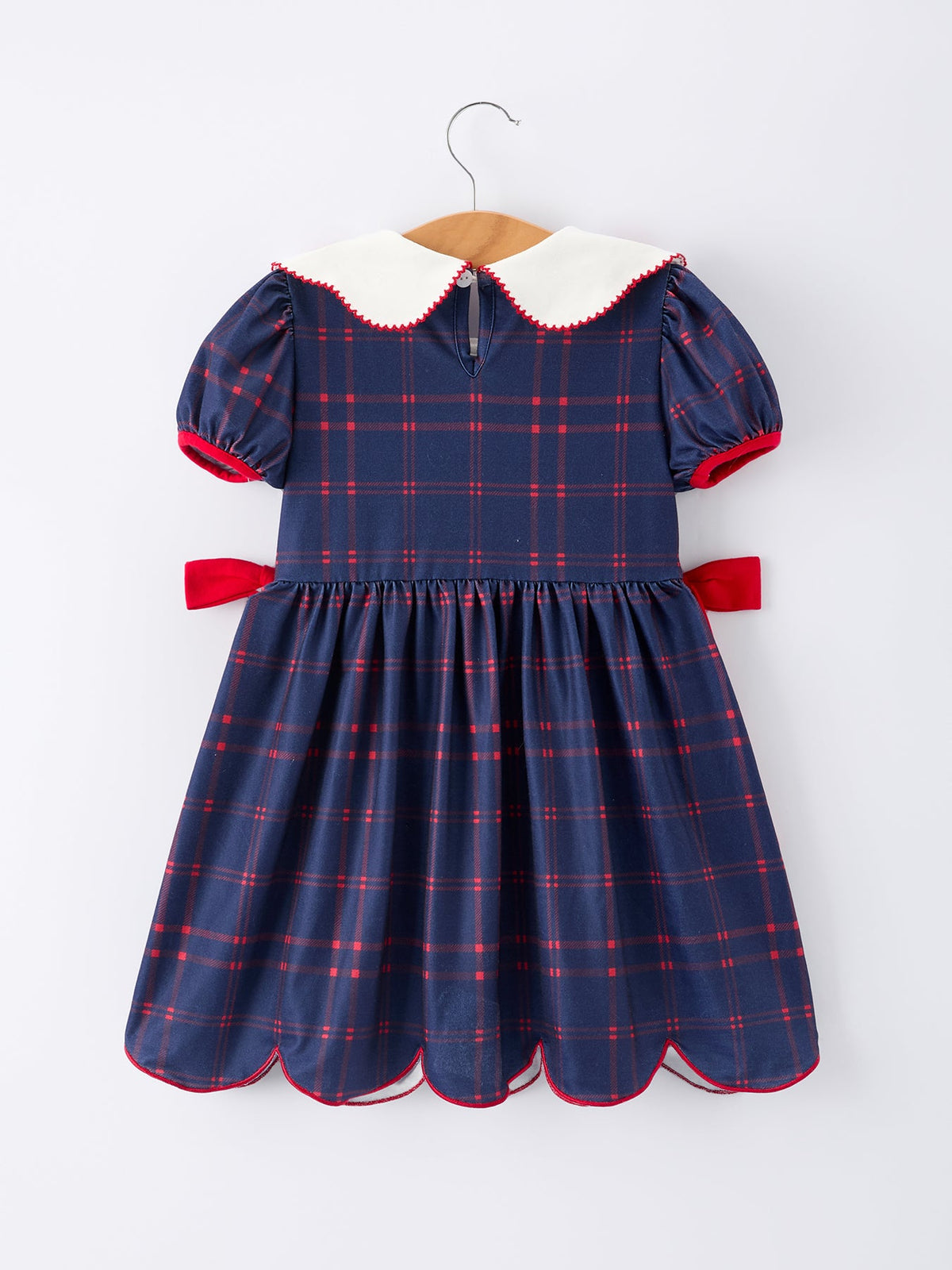 Girl wearing an organic apple plaid dress with scallop hem and bow, perfect for back to school.