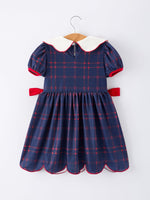 Girl wearing an organic apple plaid dress with scallop hem and bow, perfect for back to school.