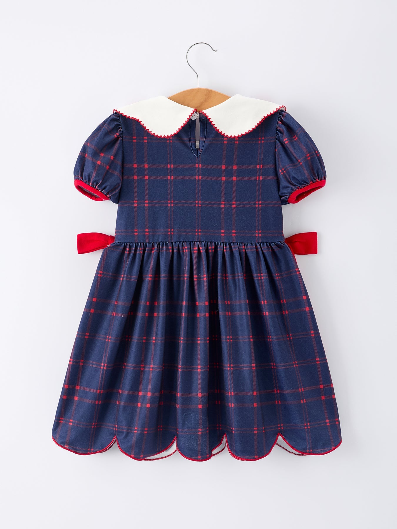 Girl wearing an organic apple plaid dress with scallop hem and bow, perfect for back to school.