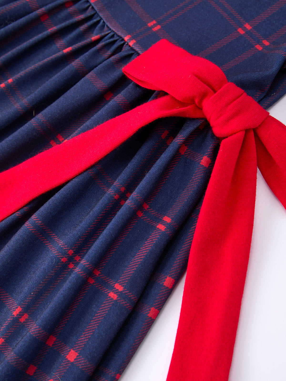 Girl wearing an organic apple plaid dress with scallop hem and bow, perfect for back to school.