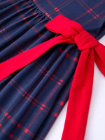 Girl wearing an organic apple plaid dress with scallop hem and bow, perfect for back to school.