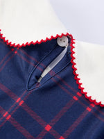 Girl wearing an organic apple plaid dress with scallop hem and bow, perfect for back to school.