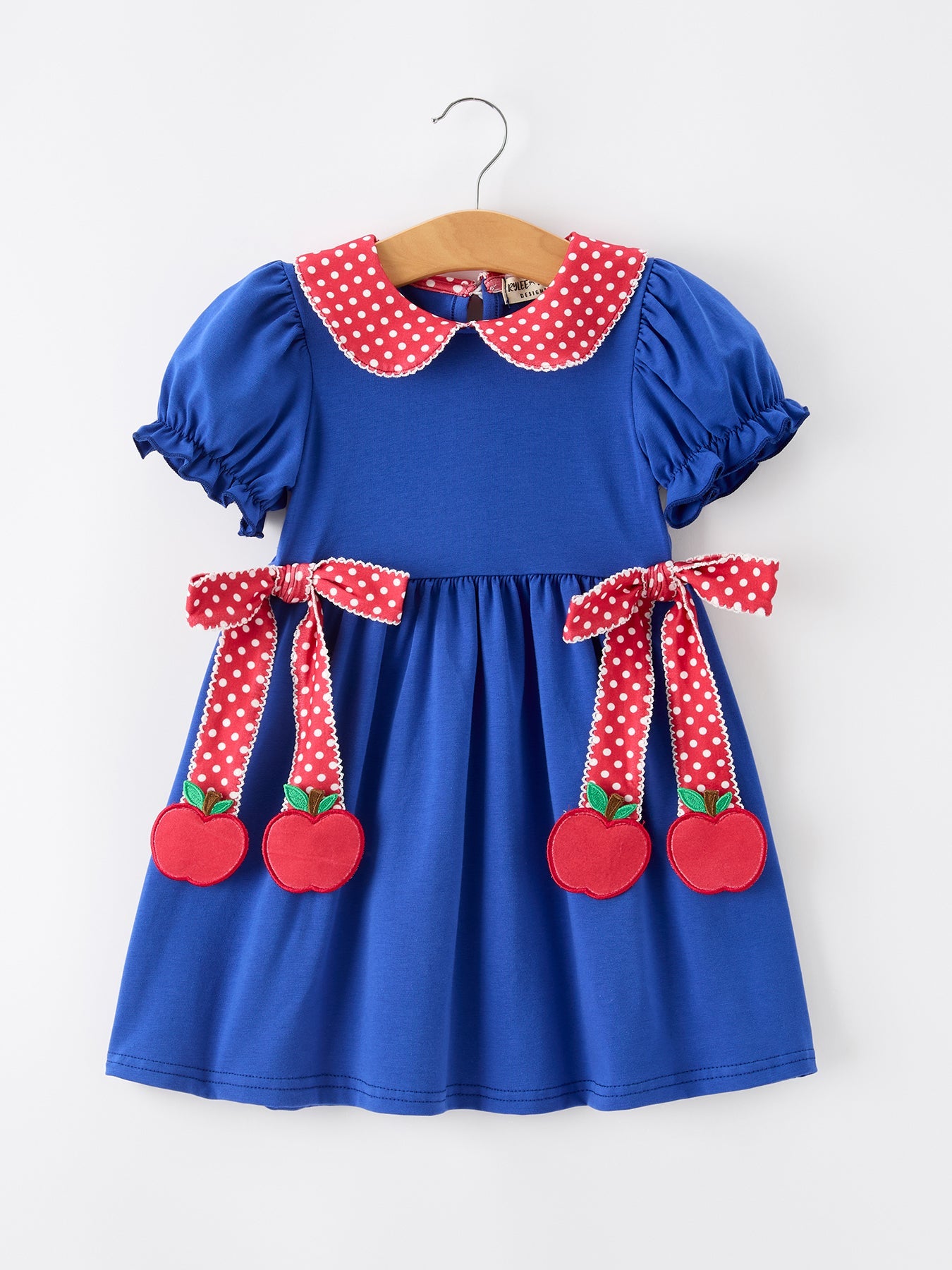 Young girl wearing a Rylee Faith apple polka dot dress with a petal collar and bow detail, perfect for back to school.