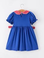 Young girl wearing a Rylee Faith apple polka dot dress with a petal collar and bow detail, perfect for back to school.