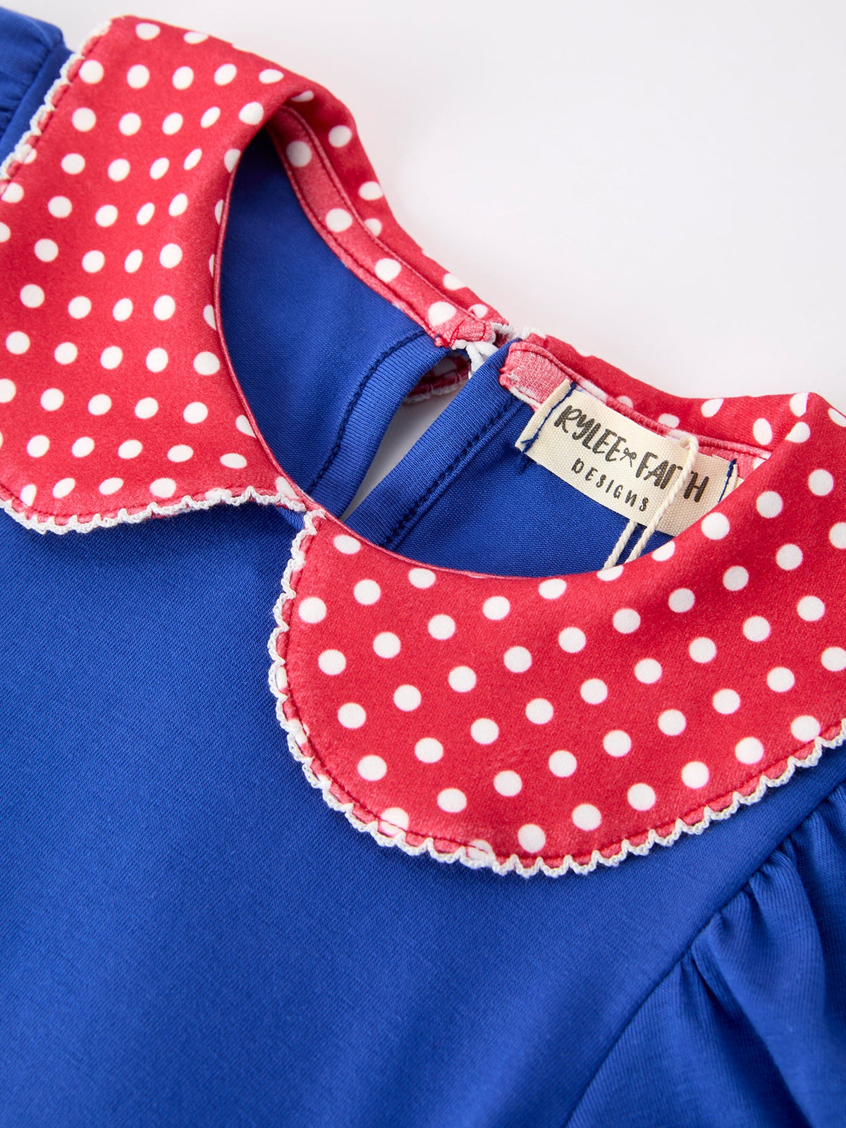 Young girl wearing a Rylee Faith apple polka dot dress with a petal collar and bow detail, perfect for back to school.