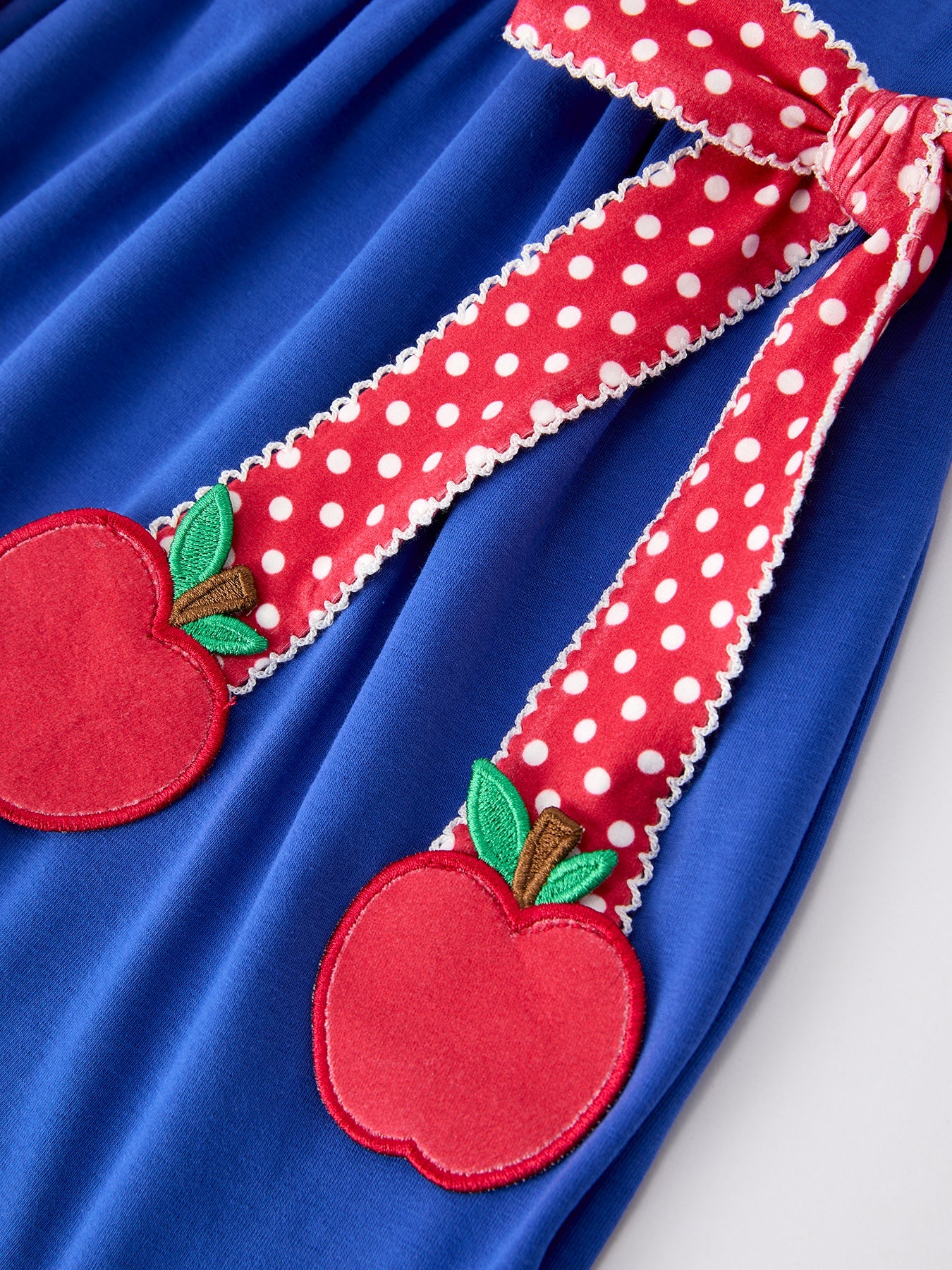 Young girl wearing a Rylee Faith apple polka dot dress with a petal collar and bow detail, perfect for back to school.