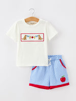 Boy wearing a white short-sleeve top with apple pencil embroidery and navy blue shorts, perfect for back to school.