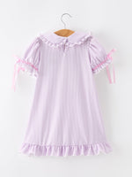 Young girl wearing a purple dress with a pencil applique, petals collar, and ruffled hem.