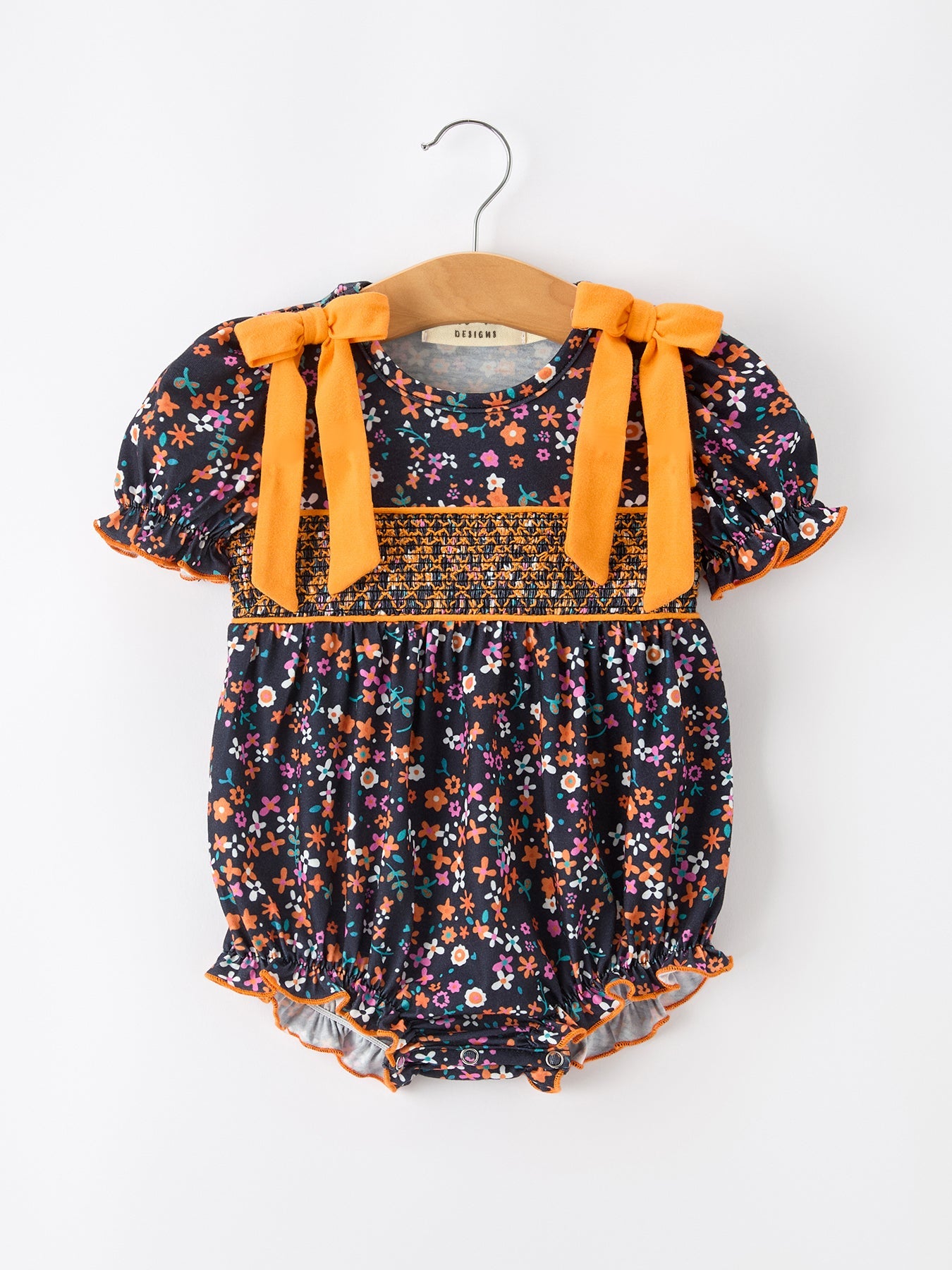 Baby bubble romper in orange floral print with smocked bodice, puff sleeves, orange bow shoulder details, and ruffle legs.