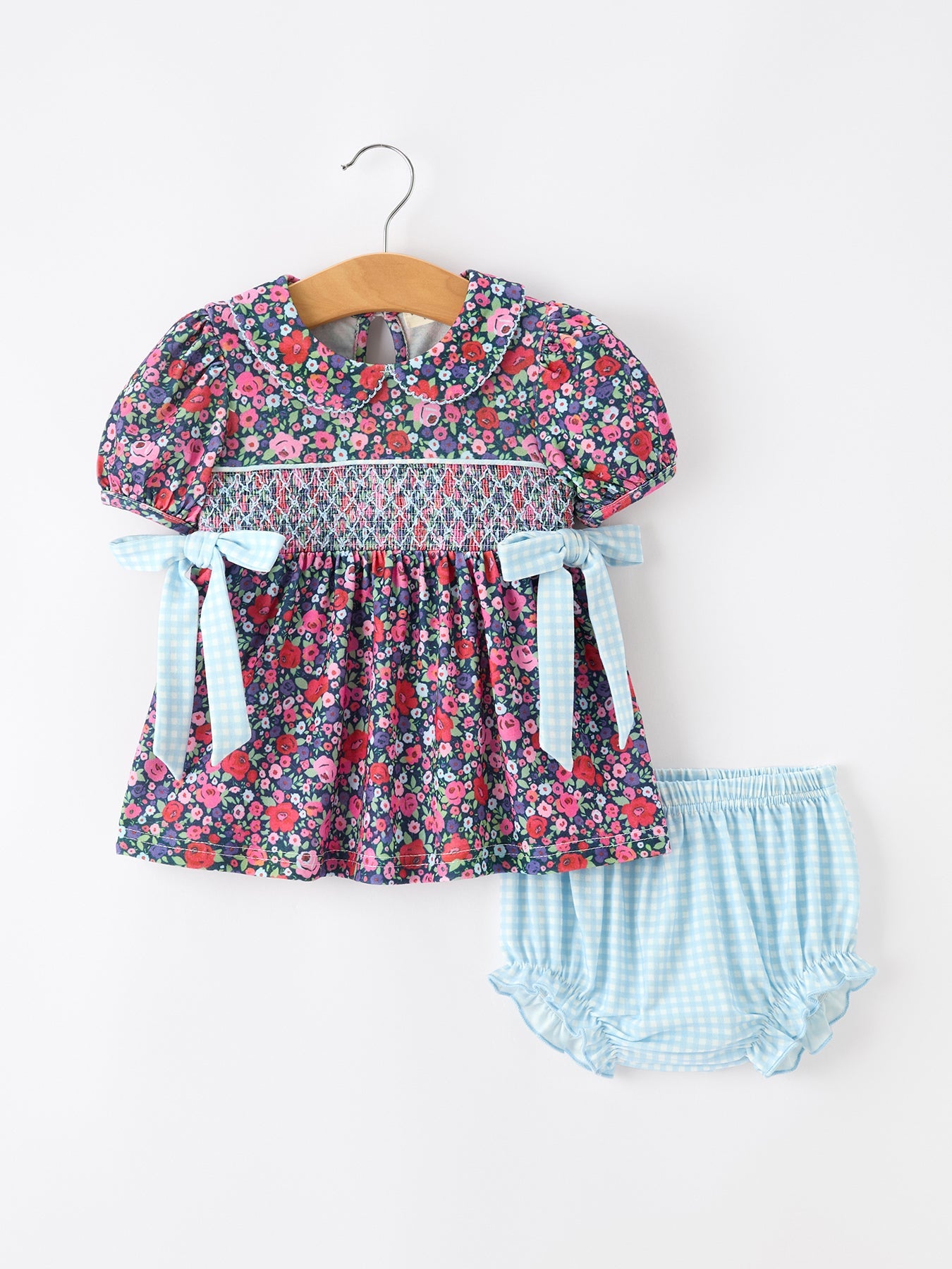 Girl two-piece set with floral smocked bodice, puff sleeves, Peter Pan collar, and light blue gingham bloomers with bows.