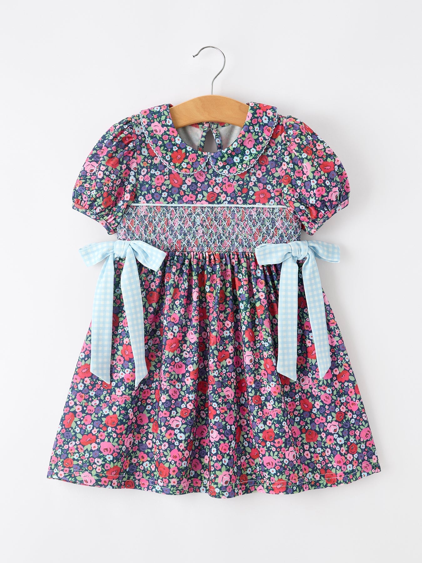 Floral girl dress with blue gingham bow accents, smocked bodice, puff sleeves, and a flowy skirt