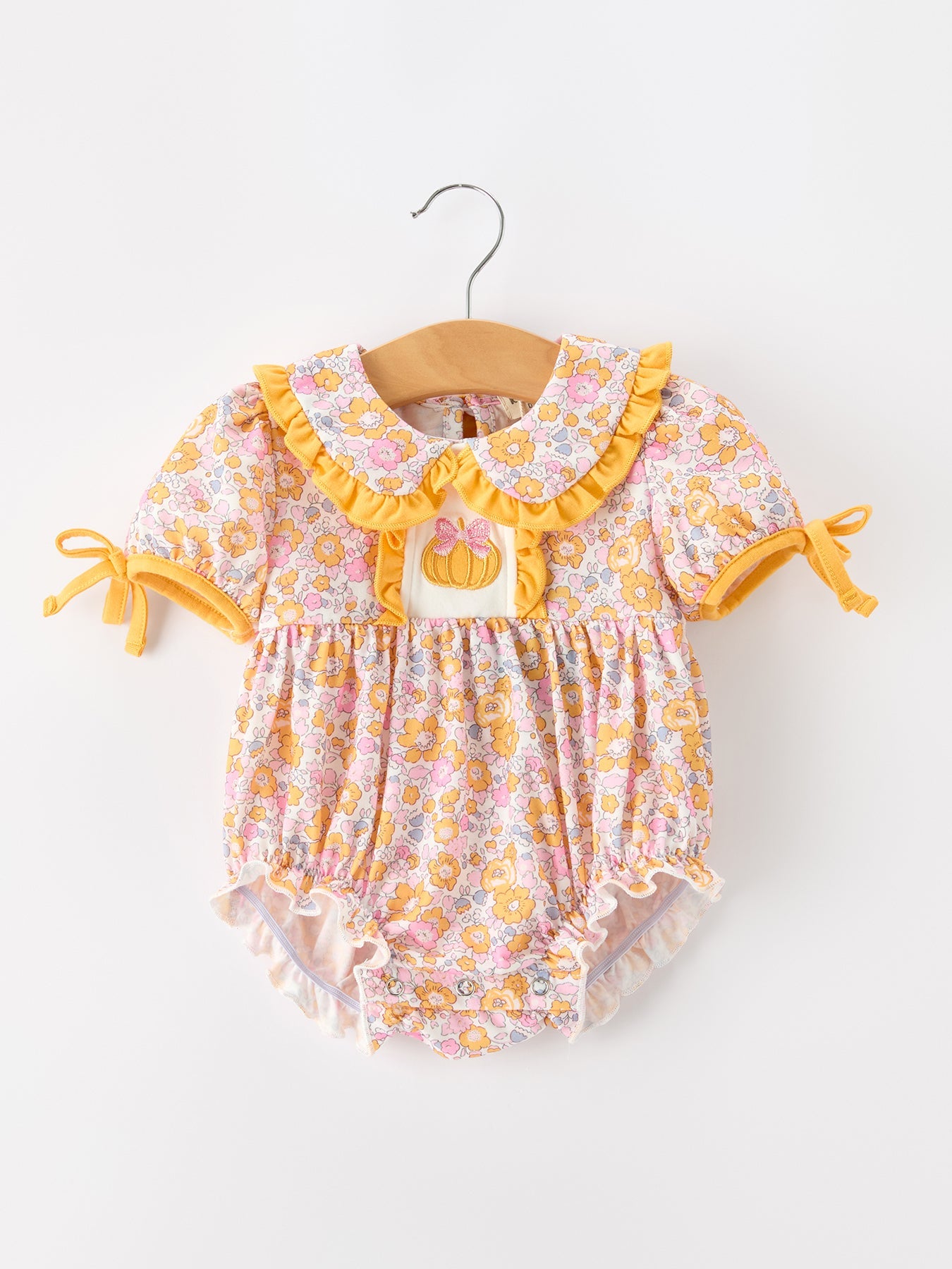 Baby bubble romper in pastel floral print with a pumpkin applique, scalloped ruffle collar, puff sleeves, and ruffle leg