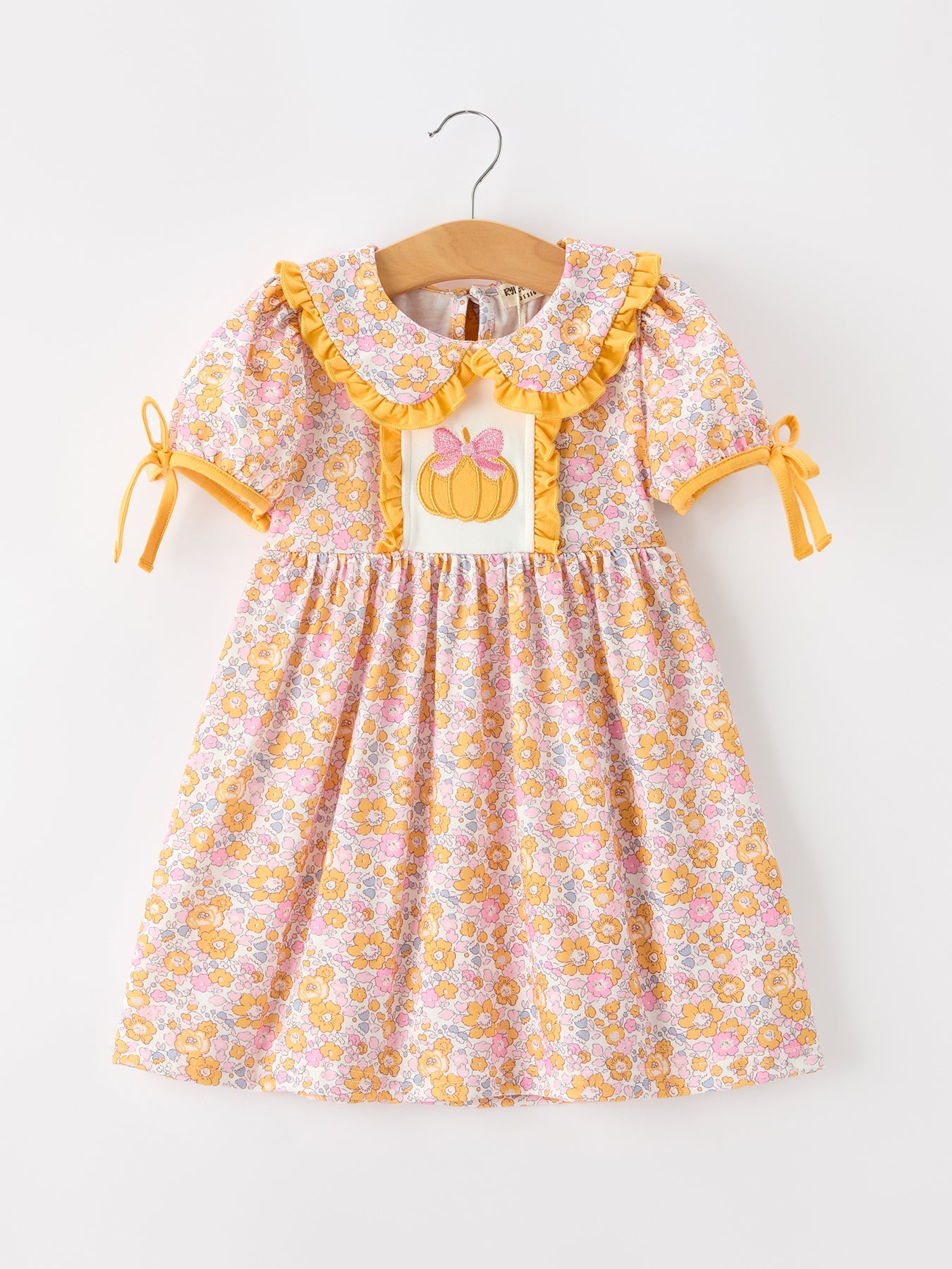 Girls dress with pastel floral print, pumpkin applique panel, ruffle collar, puff sleeves, and side bow accents.