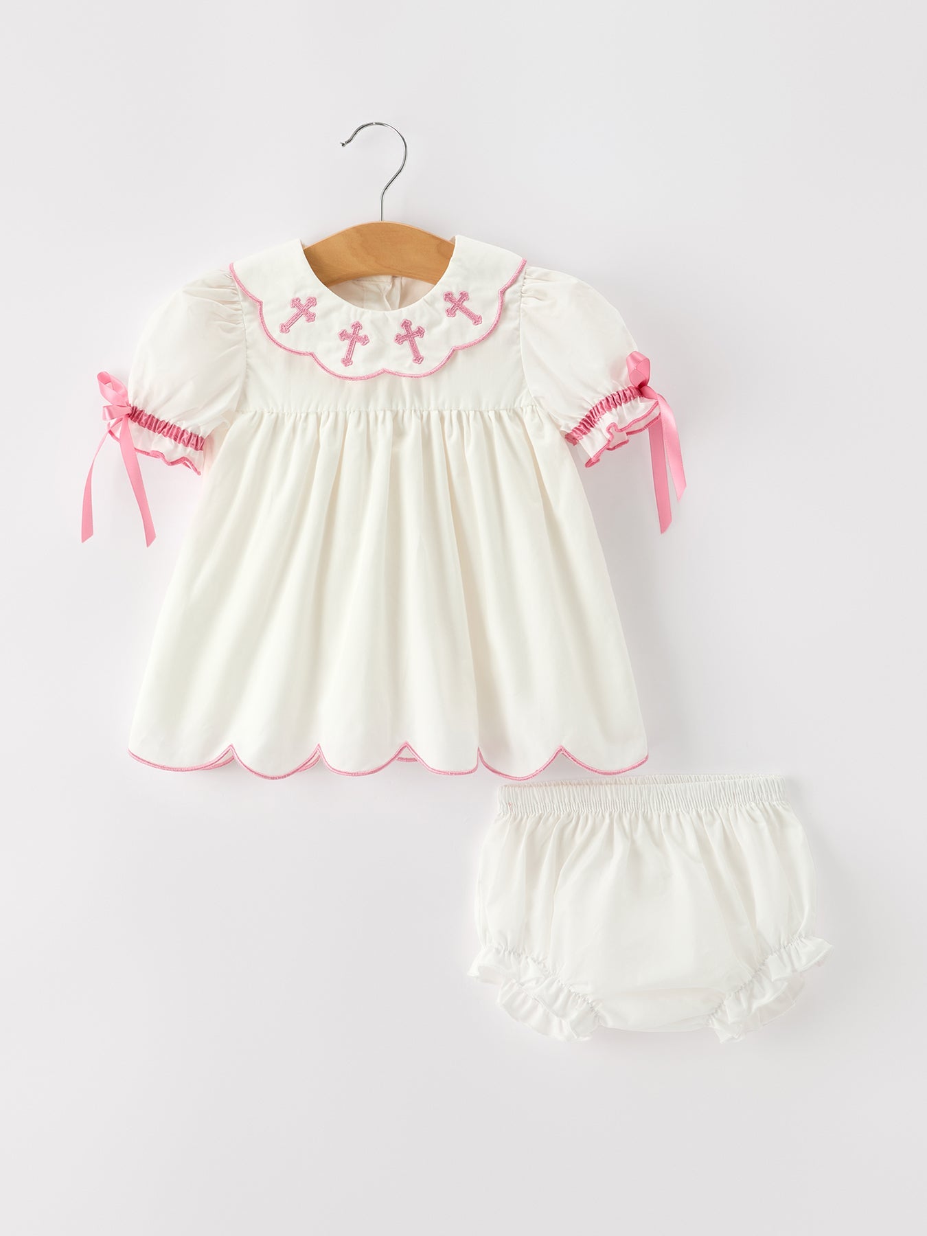 Ivory bishop christening set with pink cross embroidery, scalloped collar, puff sleeves, ribbon ties, and matching bloomers.