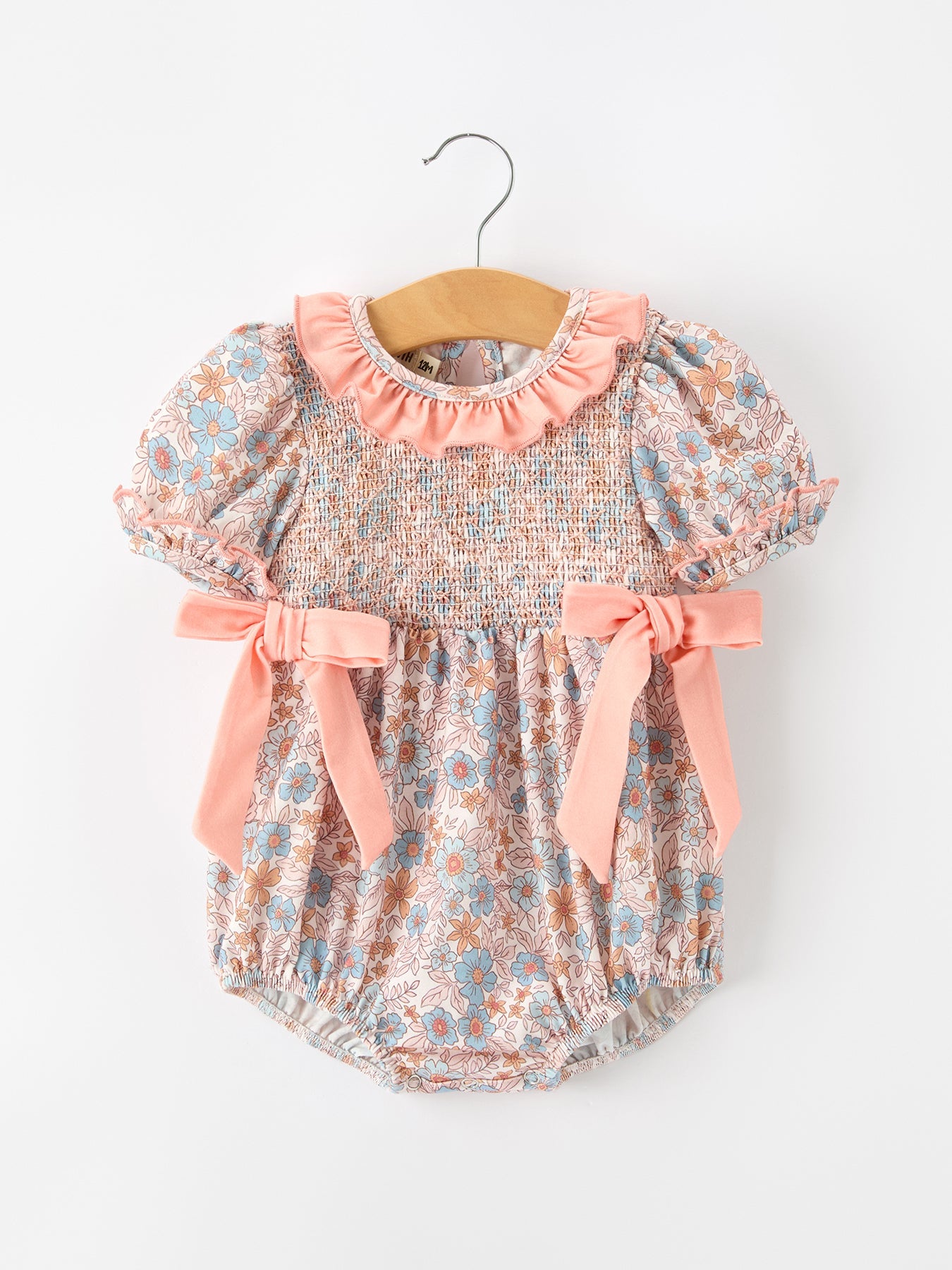 Baby romper with fall floral print, smocked bodice, ruffle neckline, and bow accents.