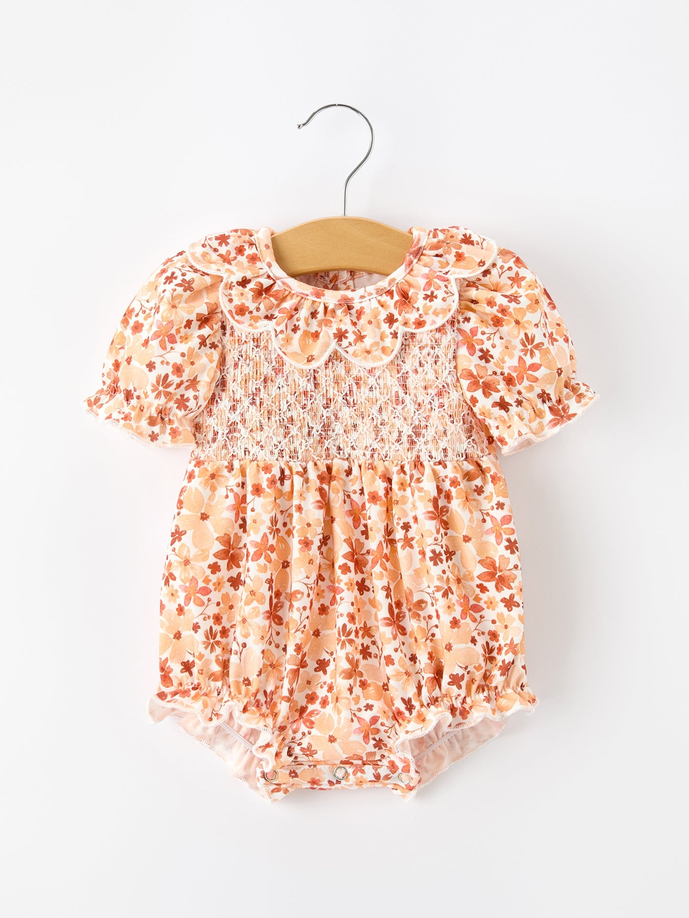 Baby romper in rust floral print with smocked front, puff sleeves, and a petal collar.