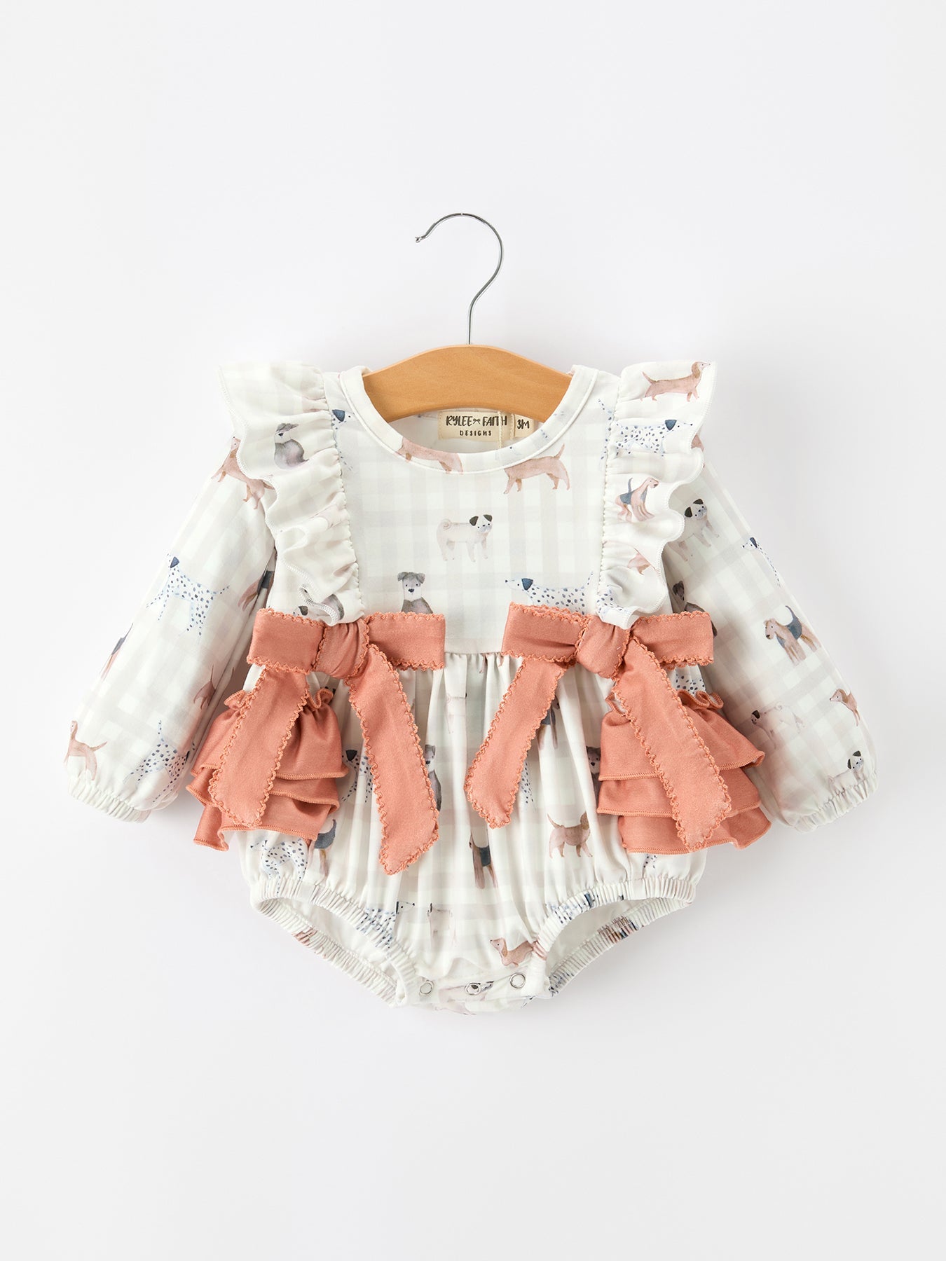 Girls long sleeve romper with a dog print over fall plaid, trimmed with bows and ruffle details.