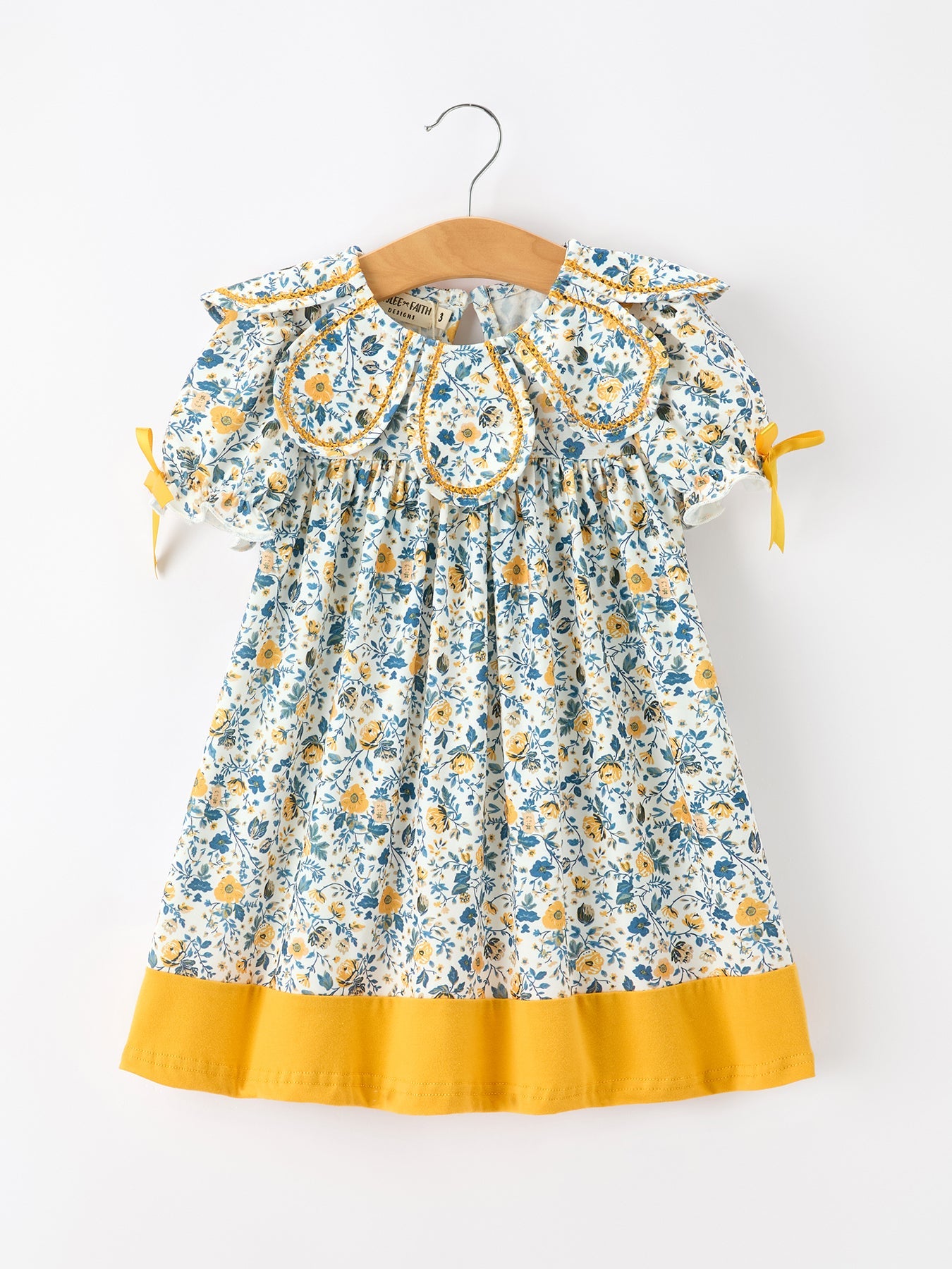 Girls dress with blue and yellow floral print, Peter Pan collar, puff sleeves with yellow ribbon ties, and yellow hem.