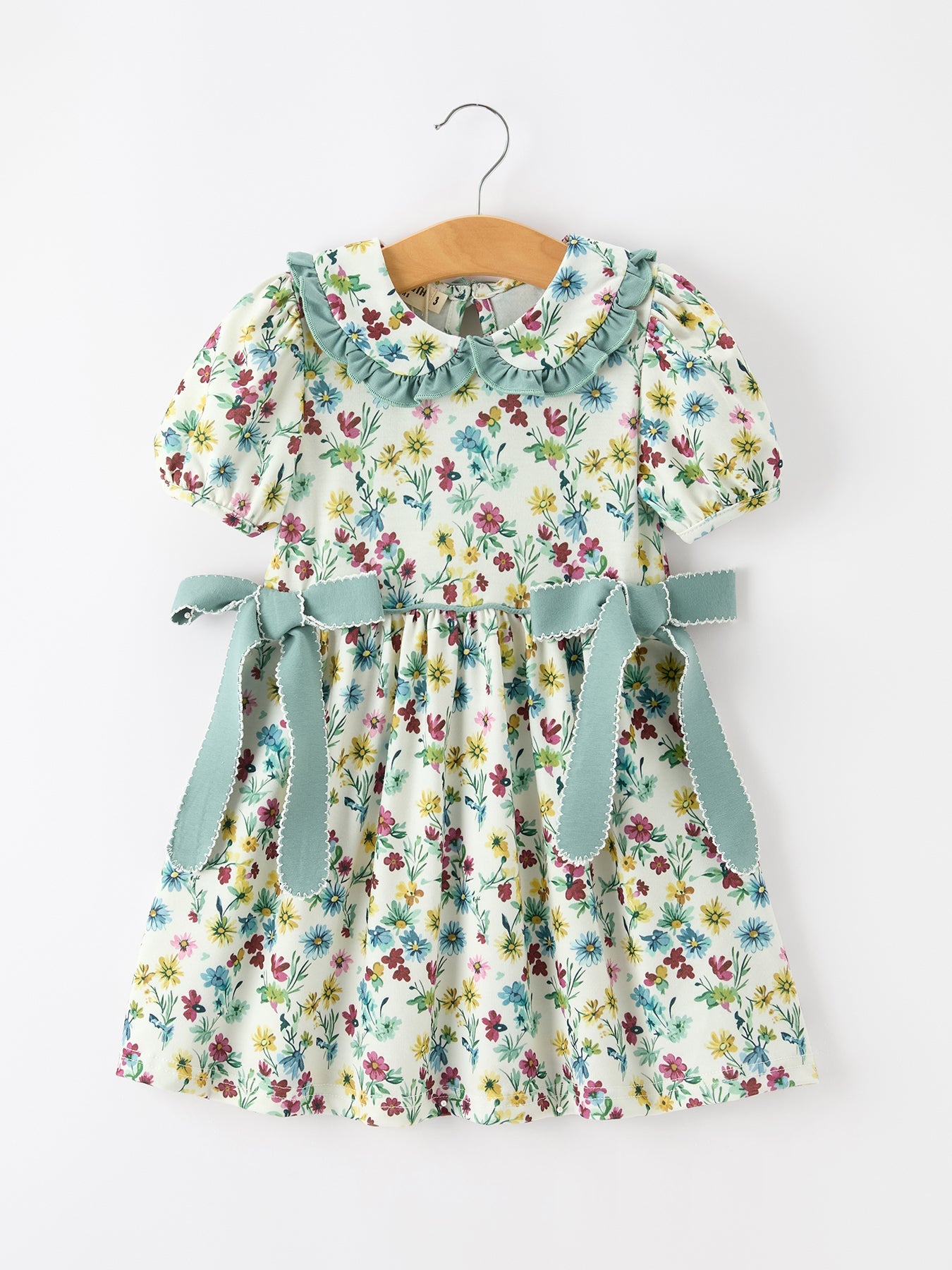 Cream floral girls' dress with green petal collar, waist bows, puff sleeves, and gathered skirt.