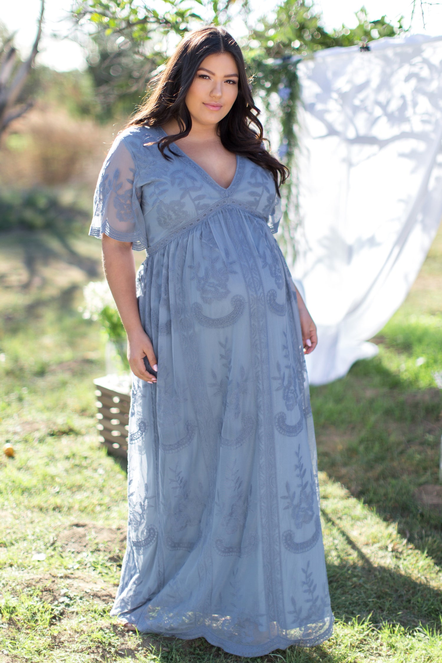 PinkBlush Plus size maternity maxi dress in blue with lace mesh overlay, modeled on a pregnant woman.